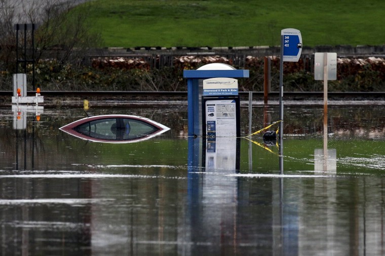 Image: A bus stop and a car sit in the flooded waters of the Stillaguamish River in Stanwood, Washington