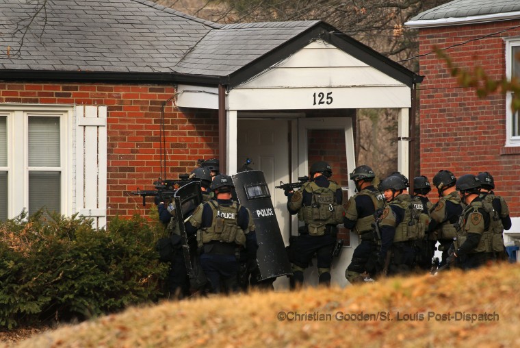 After months of peaceful protests and the sense of calming in the community, tensions rose again when a police officer was shot during a large protest outside the Ferguson police department. A manhunt ensued. The following day, a police tactical unit enters a home in the 100 block of Dade Ave. in Ferguson in March 2015, in an unsuccessful search. Withing days, police eventually caught the individual responsible without incident and announced that his motives had nothing to do with the protests. The shooter's intended target was someone he knew who was outside the police station.