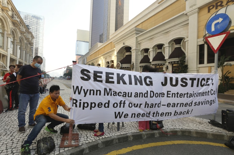 Image: A protester adjusts a banner during a demonstration by investors of Dore Holding's VIP room, outside Wynn Macau in Macau