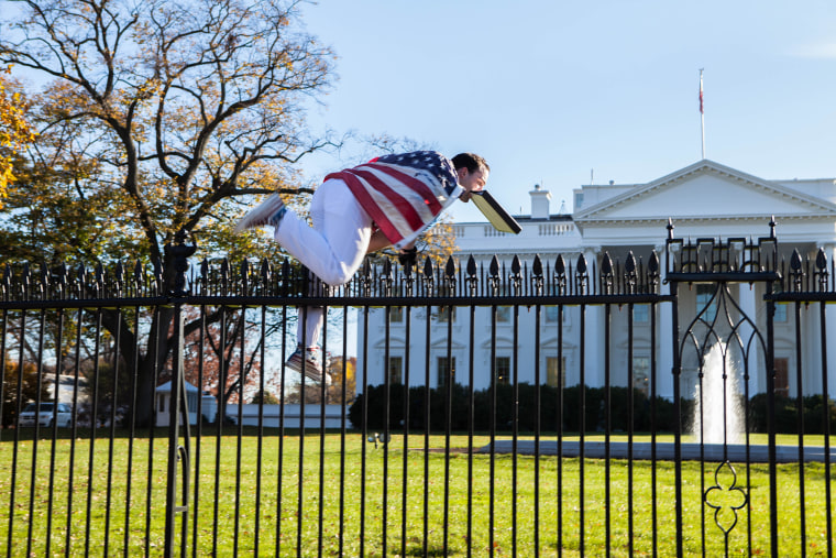 A man draped in American flag climbs over the fence surrounding the White House grounds, Thursday. Nov. 26, 2015.