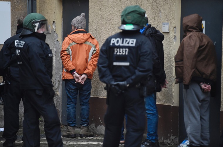 Image: Policemen stand next to handcuffed refugees at the former airport Tempelhof