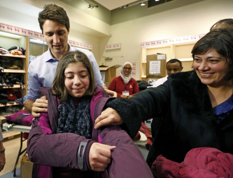 Image: Canada's Prime Minister Justin Trudeau helps a young Syrian refugee try on a winter coat after she arrived with her family from Beirut at the Toronto Pearson International Airport