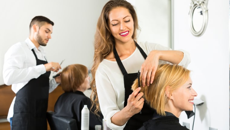 Smiling client sitting in a hair salon while hairdresser is combing her hair. Focus on client; Shutterstock ID 301639736; PO: TODAY.com