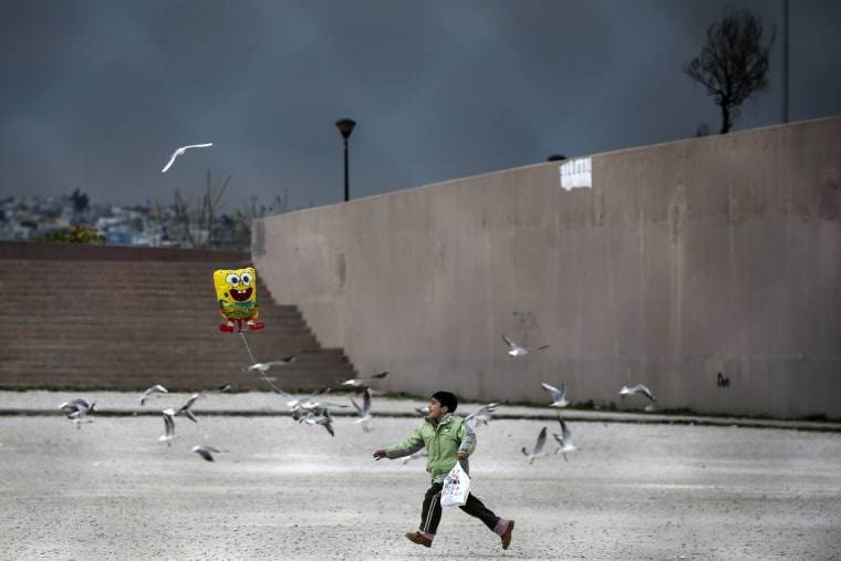 Image: A migrant boy runs while holding a balloon outside the Tae Kwon Do stadium at the southern suburb of Faliro in Athens