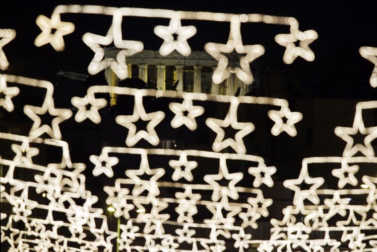 Image: The spotlit ancient Parthenon temple on the Acropolis appears behind strings of Christmas lights in central Athens