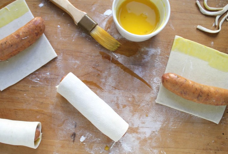 Photo 2: How to Make Sausage Puffs: Brush squares of puff pastry with egg yolk. Place the sausage on the bottom edges and roll up the pastry, pressing the ends to seal