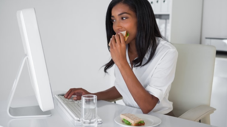 Businesswoman eating a sandwich at her desk in her office.