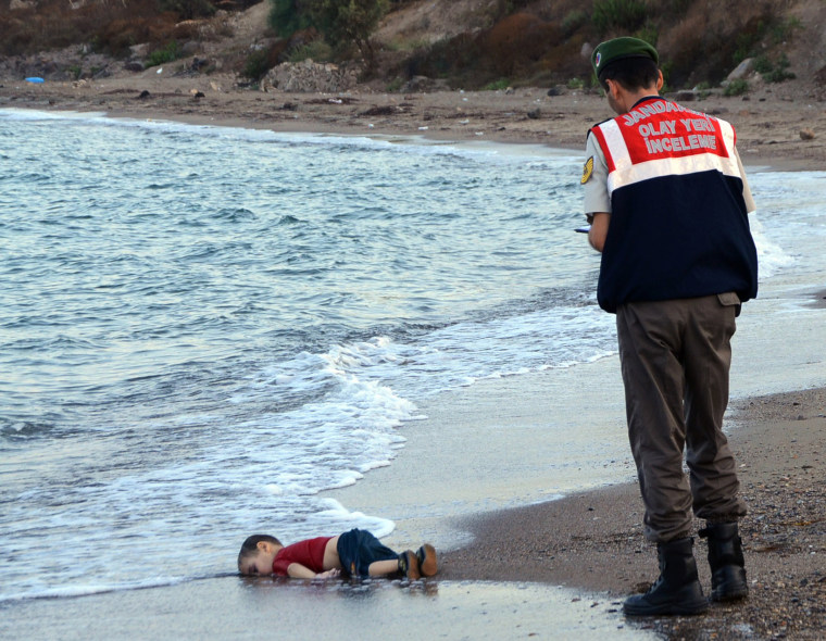 Image: A paramilitary police officer investigates the scene before carrying the lifeless body of 3-year-old Aylan Kurdi
