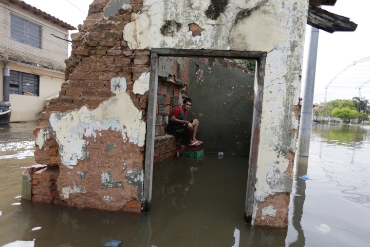 Image: A man sits near houses partially submerged in flood waters in Asuncion
