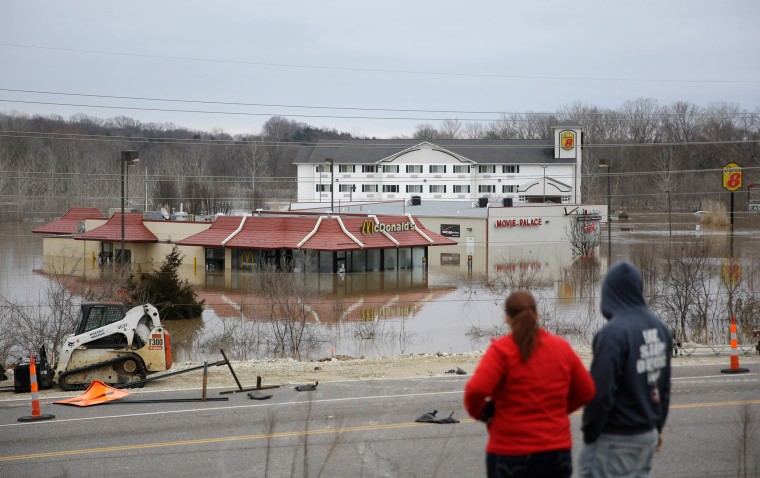 Image: People stand on a hill to get a better look at floodwater