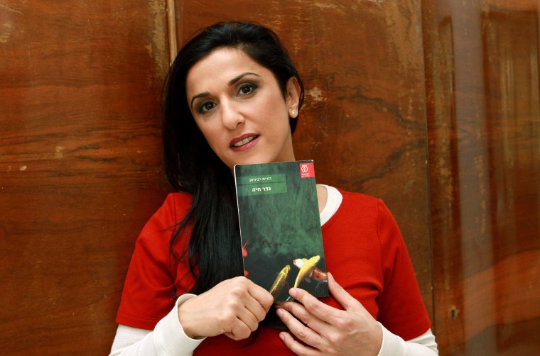 Image: Israeli author Dorit Rabinyan poses with her Hebrew-language novel titled "Gader Haya"