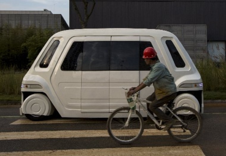 Image: Worker rides bike past driverless vehicle
