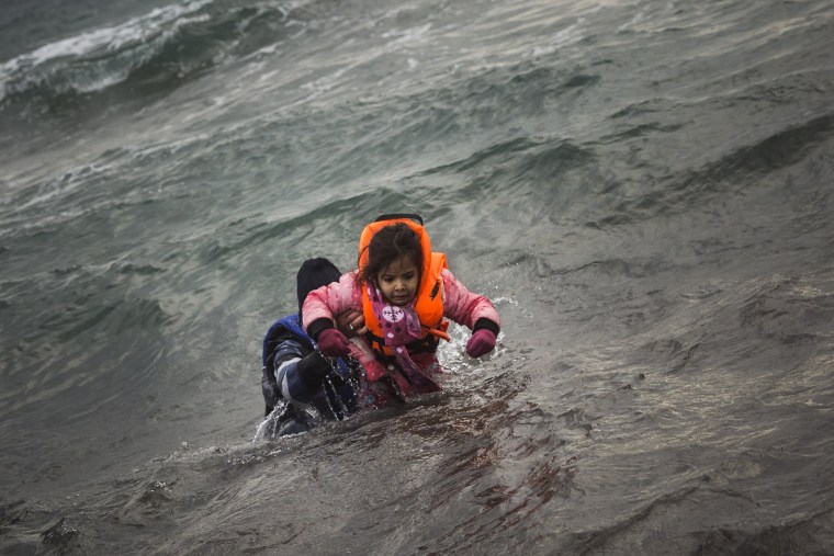 Image: A man carries a child as they try to reach the shore on the Greek island of Lesbos