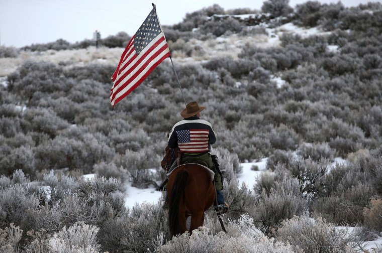 Image: Dwayne Ehmer carries an American flag as he rides his horse on the Malheur National Wildlife Refuge