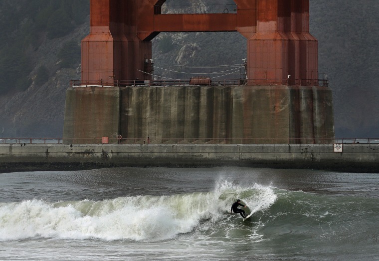 Image: A surfer rides a wave underneath the south tower of the Golden Gate Bridge