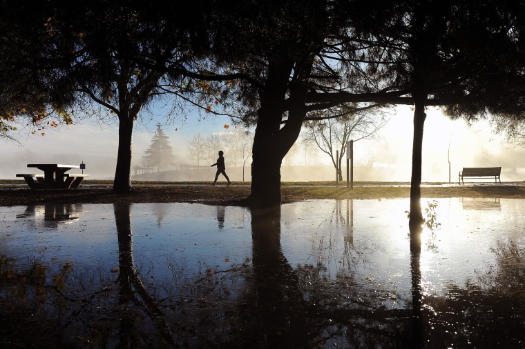 Image: A walker takes advantage of the clearing skies to stroll past rain puddles at Lake Balboa Park
