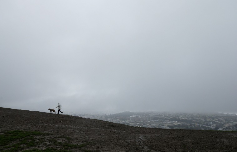 Image: A man walks a dog under rain clouds atop Bernal Heights Hill in San Francisco