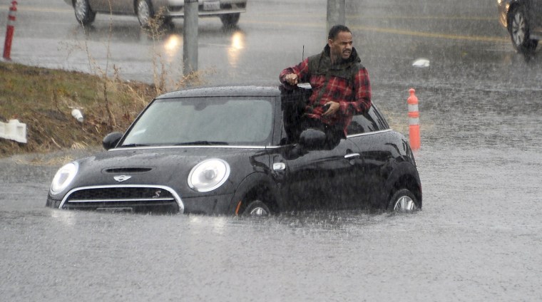 Image: A driver climbs out of a window of his car after driving onto a flooded road in Van Nuys