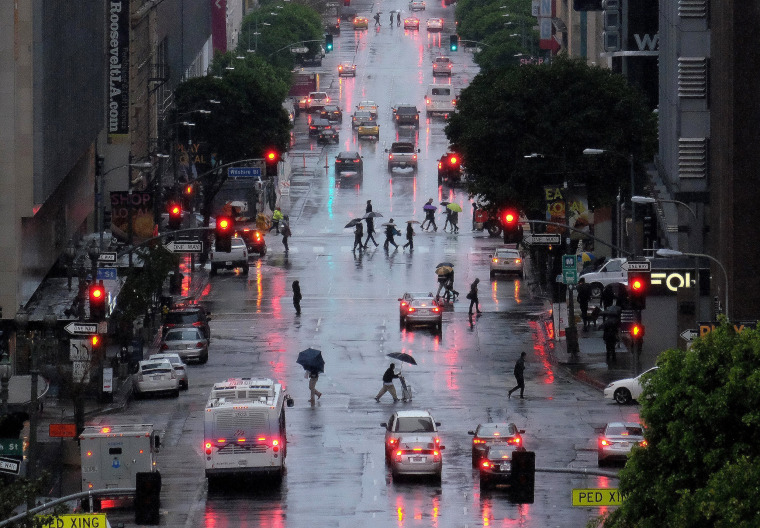Image: Pedestrians, cover up from heavy El Nino rains, cross Flower Street in downtown Los Angeles