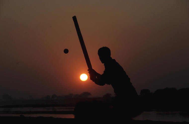 Image: A man is silhouetted against the setting sun as he plays cricket near the banks of the Ravi river in Lahore