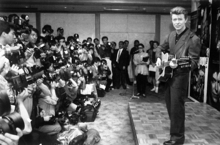 Image: Bowie plays an acoustic guitar at a press conference in Tokyo on May 19, 1990.