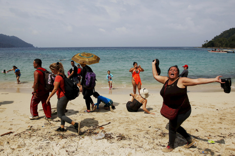 Image: A Cuban migrant shouts \"Cuba\" after arriving to the beach after crossing the border from Colombia through the jungle as tourist stand by in La Miel, in the province of Guna Yala, Panama