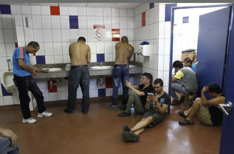 Image: Cuban migrants use their cell phones in a bathroom at the border between Costa Rica and Nicaragua in Penas Blancas