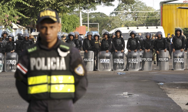 Image: Nicaraguan riot police stand behind a Costa Rican police officer at a border post with Nicaragua in Penas Blancas