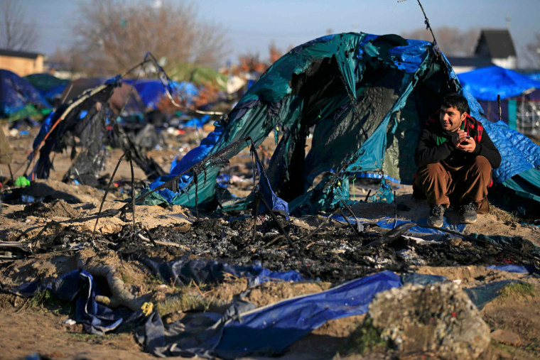 Image: An Afghan migrant sits in front of a burnt dismantled shelter in the camp known as the \"Jungle\" in Calais