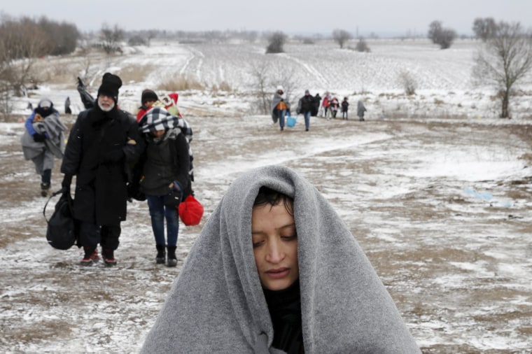 Image: Migrants walk through a frozen field after crossing the border from Macedonia