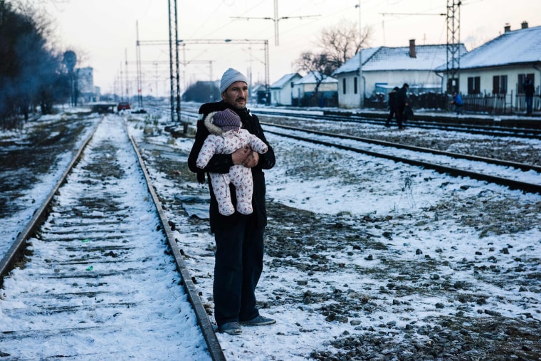 Image: A man holds his baby while waiting with other migrants and refugees at a train station in the Presevo