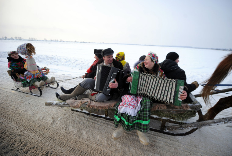 Image: A man and a woman play their accordions and sing as they ride a horse drawn sleigh celebrating the Kolyada holiday