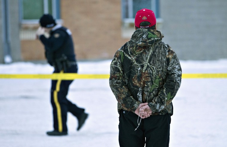 A man holds a rosary as police investigate the scene of a shooting at the community school in La Loche, Saskatchewan, on Saturday, Jan. 23, 2016, a day after the violence.