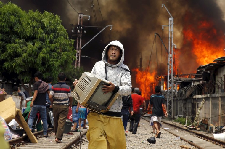 Image: A man carries a television away from a fire in a slum area next to railway tracks in Kampung Bandan, North Jakarta, Indonesia