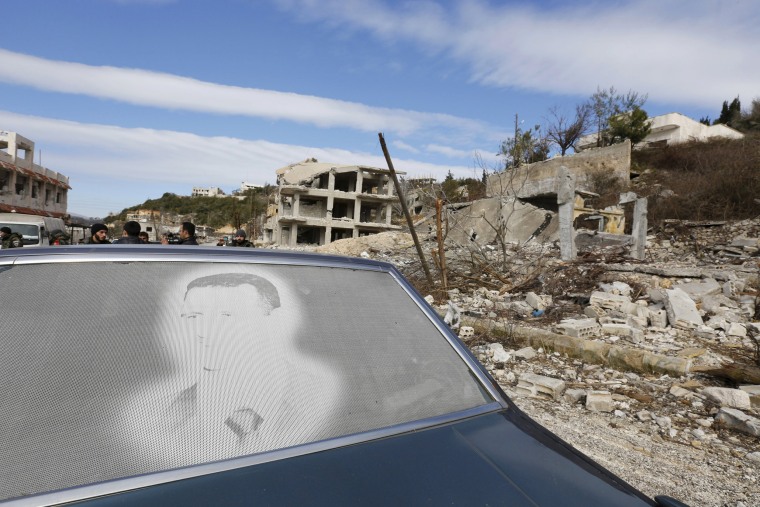 Image: An image of Assad is seen on a car parked in front of damaged buildings in the town of Rabiya