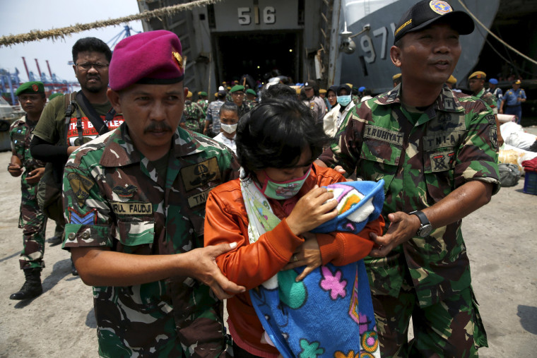 Image: Indonesian Navy personnel assist a member of Gafatar sect disembark from the KRI Teluk Banten naval ship