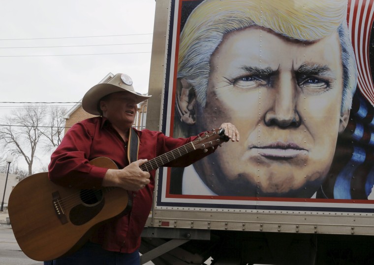 Image: Moss tunes his guitar before performing his song about Trump in front of a truck featuring Trump in Des Moines