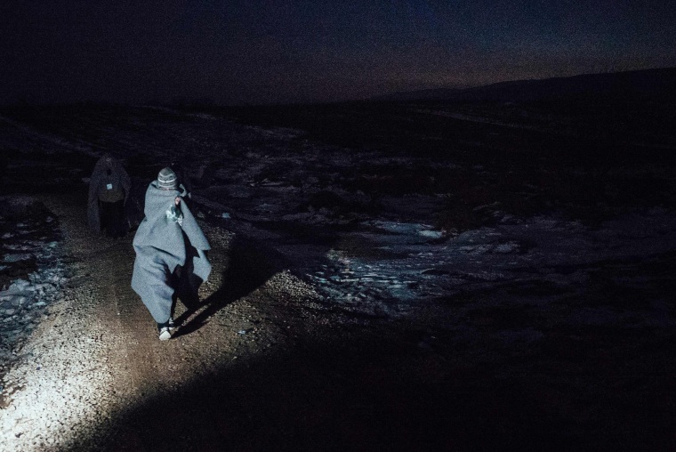 Image: A migrant uses his sleeping blanket to keep warm as he walks after crossing the Macedonian border into Serbia