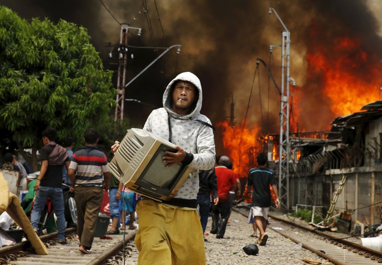 Image: A man carries a television away from a fire in a slum area next to railway tracks in Kampung Bandan, North Jakarta, Indonesia