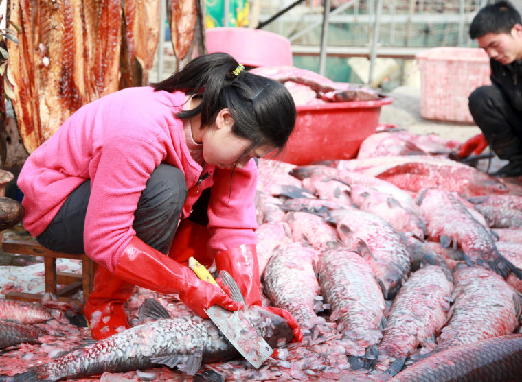 Image: A woman scales fish by the side of a lake