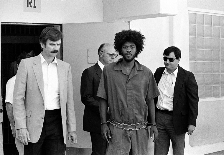 Kevin Cooper, center, a suspect in connection with the slashing death of four people in Chino, is escorted to a car for transport to San Bernadino from Santa Barbara, Calif., after he was arrested by police at Santa Cruz Island, July 31, 1983.