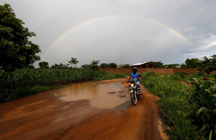 Image: Storm clouds hover as a motorcyclist rides past a field of maize after late rains near Malawi's capital Lilongwe
