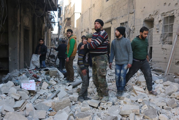 Image: A Syrian man comforts a boy amid the rubble of buildings