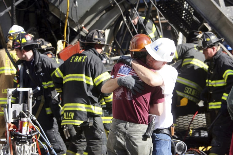 Image: Construction workers embrace as rescue crews work at the scene of a crane collapse