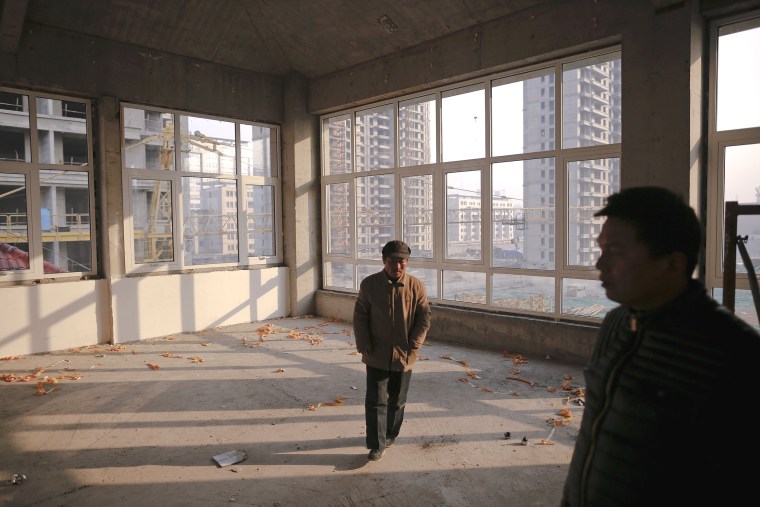Image: Migrant workers walk inside an unfinished building at the construction site of Zixia Garden development complex in Qianan, Tangshan City