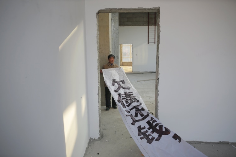 Image: A migrant worker shows a banner inside a building that is under construction as a part of Zixia Garden development complex in Qianan, Tangshan City