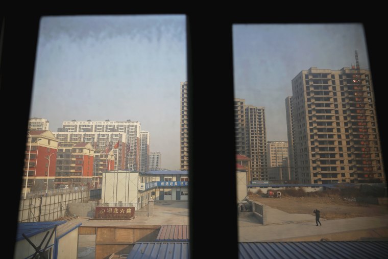 Image: A man is seen from inside the offices of a subcontractor company as he walks through the construction site of Zixia Garden development complex in Qianan, Tangshan City