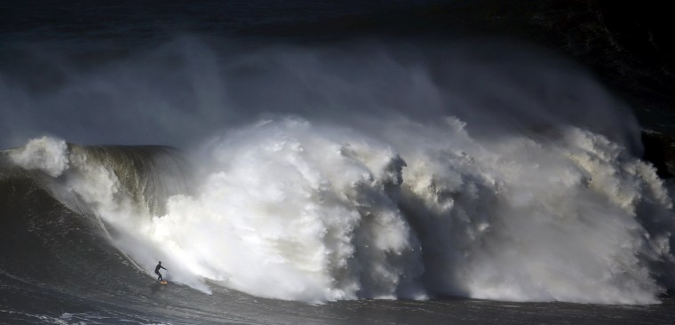 Image: A surfer drops in on a large wave at Praia do Norte in Nazare
