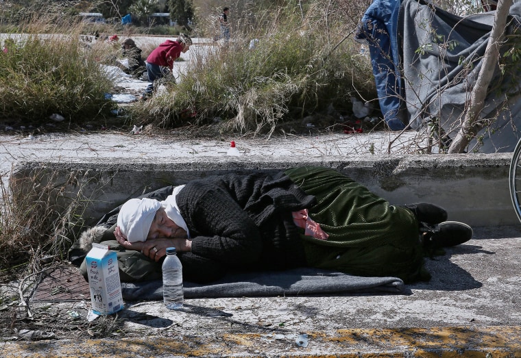 Image: An elderly migrant sleeps on the ground outside the old airport