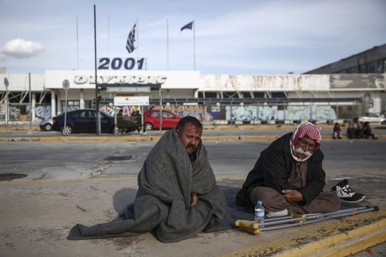 Image: Two men from Iraq sit at a parking area outside the old international airport in Athens